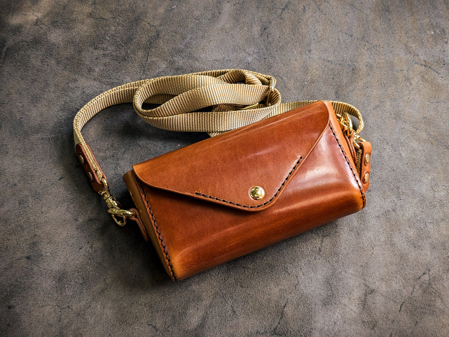 Handmade leather shoulder bag with adjustable strap and envelope-style closure, representing the studio's bag collection.