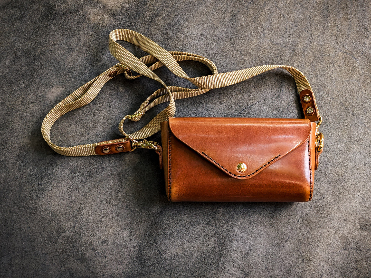 Renee crossbody bag handcrafted from vegetable-tanned leather with envelope-style flap closure, brass hardware, and adjustable canvas shoulder strap.