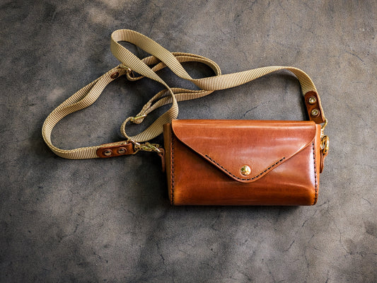 Renee crossbody bag handcrafted from vegetable-tanned leather with envelope-style flap closure, brass hardware, and adjustable canvas shoulder strap.