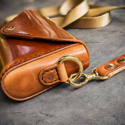 Close-up of the Renee crossbody bag featuring brass ring hardware, leather attachment tab, and edge finishing details.