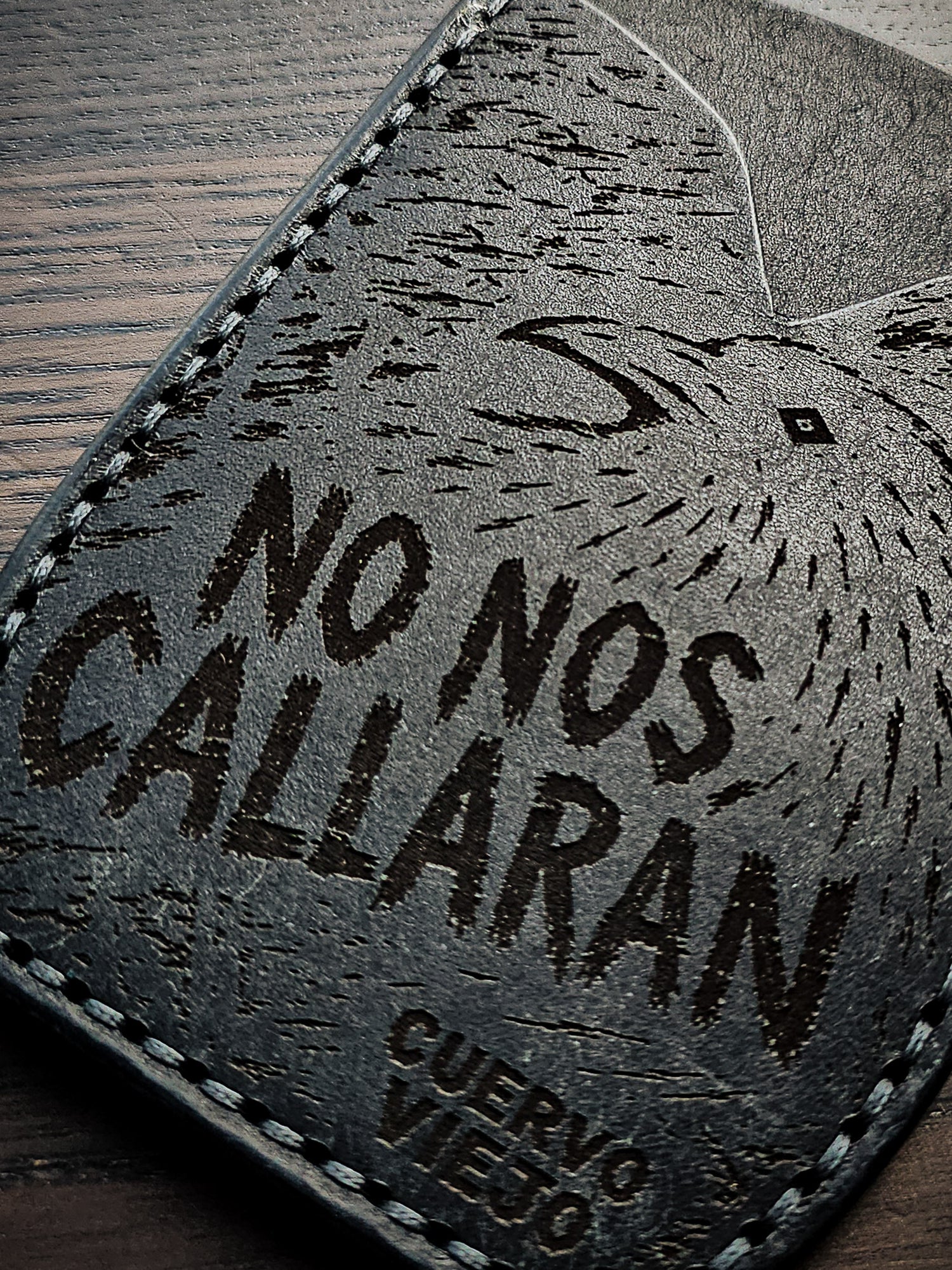 Close-up of laser-engraved black leather featuring a crow illustration and the words "No Nos Callarán" from Cuervo Viejo Studio