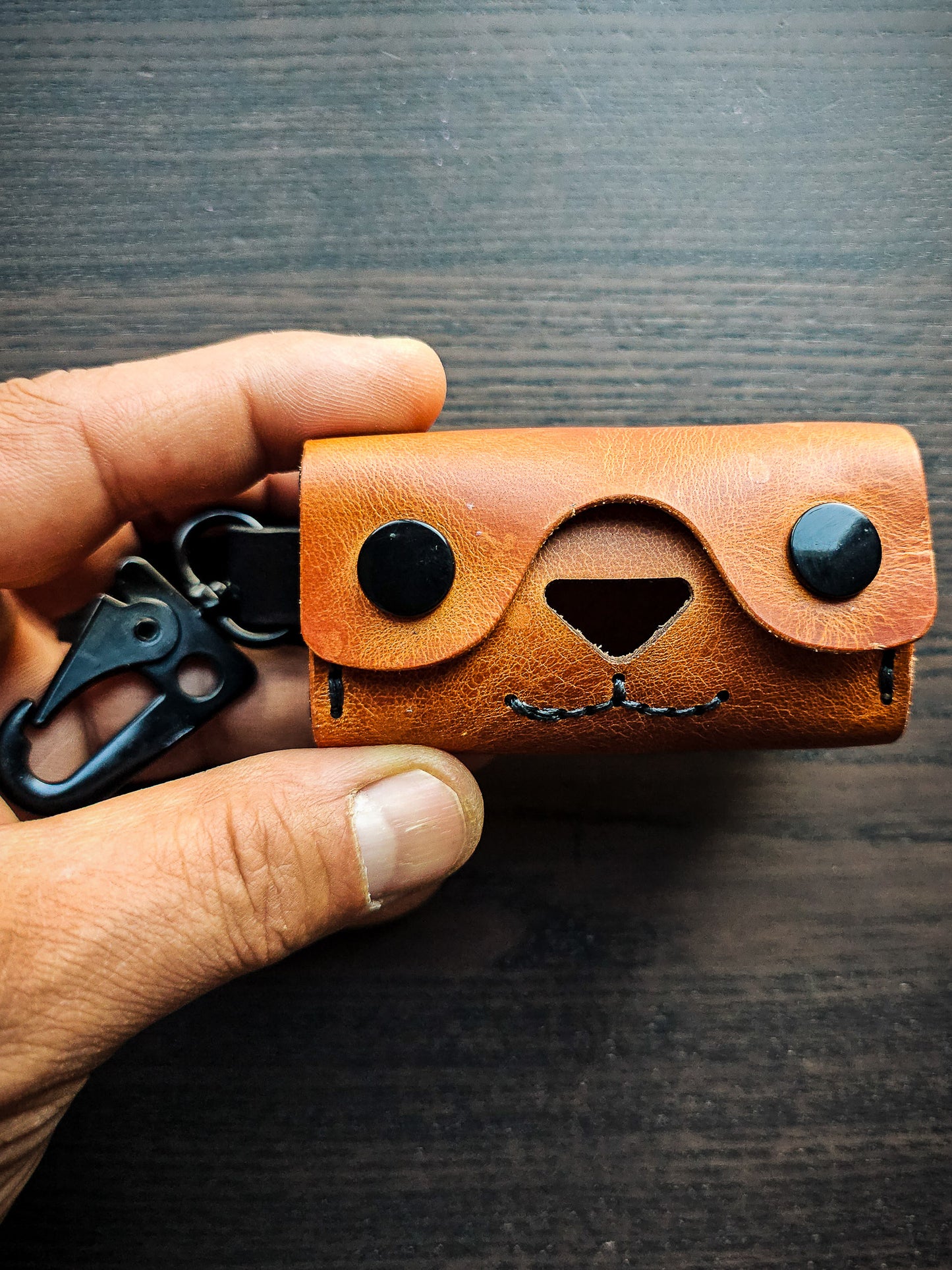Doggy Duty leather waste bag dispenser featuring a dog face design created with snap eyes, a cutout nose, stitched mouth, and blue waste bag dispensing opening.