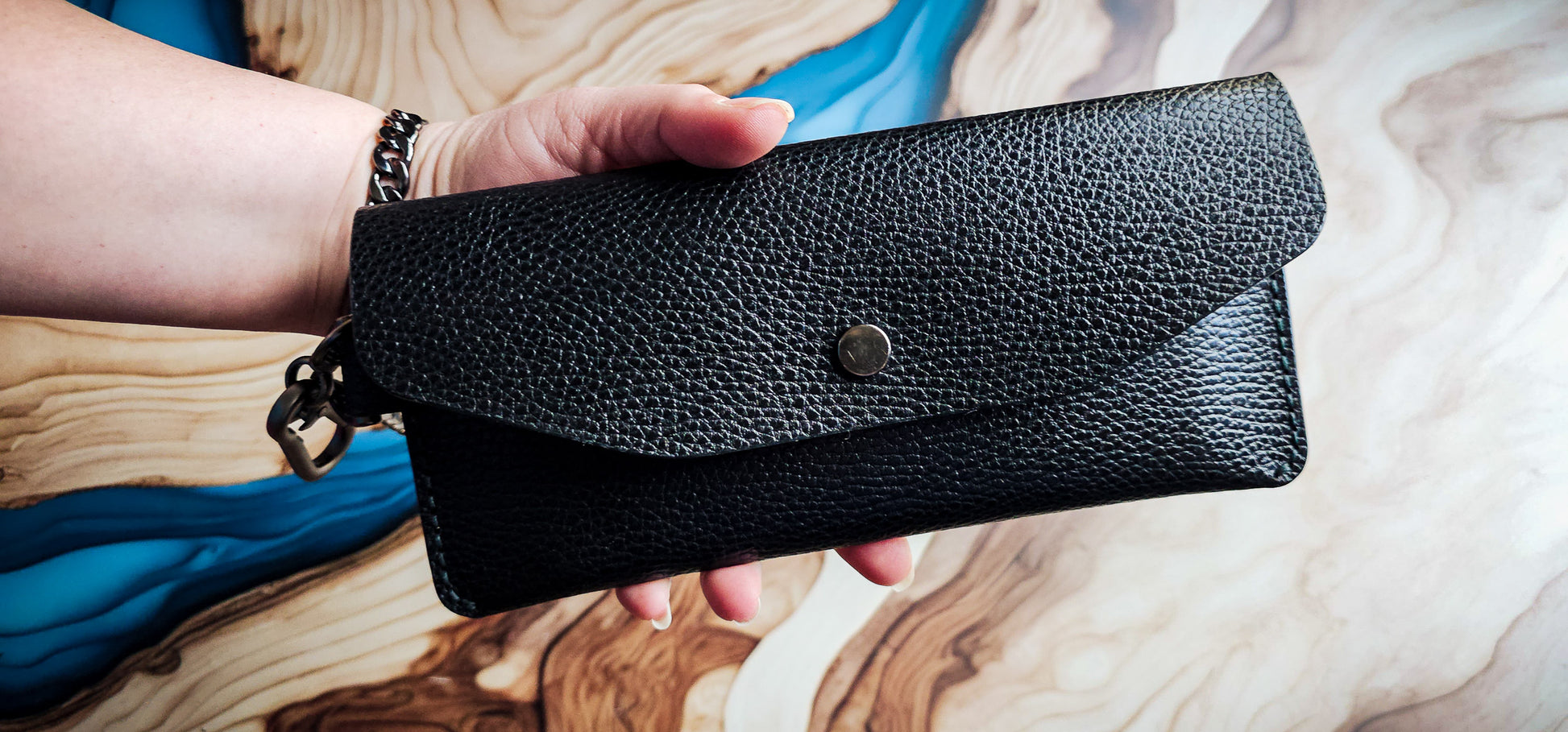 Hand holding the Delilah Clutch, showcasing the slim profile and black pebbled leather exterior.