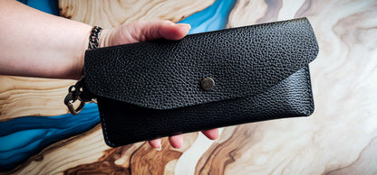 Hand holding the Delilah Clutch, showcasing the slim profile and black pebbled leather exterior.