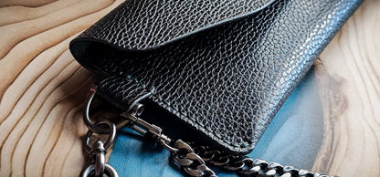 Close-up detail of the Delilah Clutch showing pebbled leather texture, edge finishing, and chain attachment.